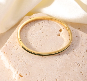 Detail eines 18K vergoldeten Armreifs mit grünen Steinen auf Stein und Seide