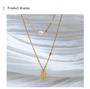 Detalle de collar doble dorado con perla y colgante ovalado de metal hecho a mano