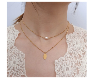 Detalle de collar doble dorado con perla y colgante ovalado 'HAND MADE'