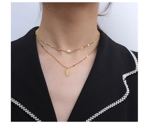 Detalle de collar de doble capa dorado con perla pequeña y colgante ovalado grabado