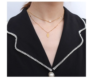 Detalle del collar doble dorado con perla y colgante grabado con HAND MADE