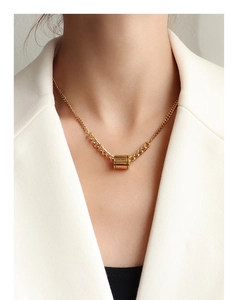 Gros plan du collier cylindre gravé doré porté avec un élégant blazer blanc cassé