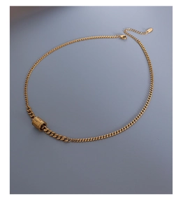 Détail de la chaîne plate dorée avec un pendentif cylindrique gravé et fermoir mousqueton