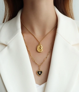 Detail of layered gold necklace with lava texture oval and black heart pendant