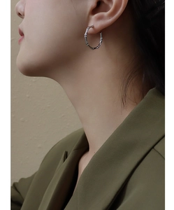 Close-up of silver bamboo texture hoop earrings on a model wearing an olive suit