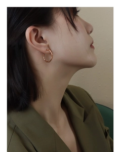 Detail view of rose gold bamboo-style hoop earrings worn by a model in lifestyle shot