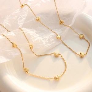 Elegante gouden hartjesketting met meerdere bedeltjes op een fijne ketting en keramiek
