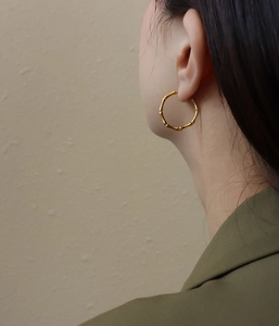 Close-up of golden bamboo-style hoop earrings on female model in warm lighting