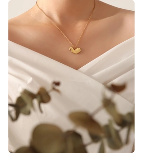 Primer plano de collar con colgante de grulla de origami dorada en modelo para mujer