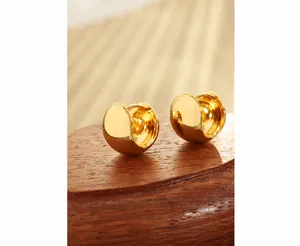 Macro shot of polished gold thick hoop earrings on dark wood display with glossy finish
