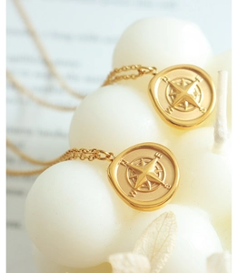 Macro shot of two gold compass coin pendants with compass engraving and fine O-chains