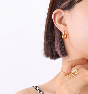 Detail shot of hollow heart-shaped gold earrings and minimalist stacked rings on model