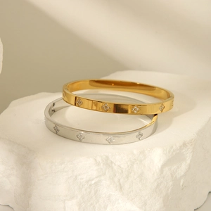 Detailed view of gold and silver four-leaf clover bangles with zircon inlay on white stone