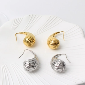 Close-up view of elegant gold and silver textured teardrop earrings on a white ceramic tray