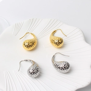 Close-up of gold and silver teardrop earrings with golf-ball texture on a white ceramic tray