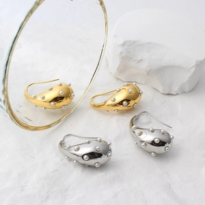 Detailed view of teardrop pearl earrings in gold and silver finish on stone background