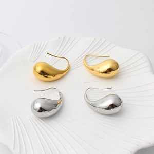 Detailed close-up of gold and silver teardrop earrings on a textured ceramic dish