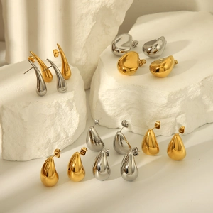 Macro detail of polished gold and silver teardrop earrings on a white stone background