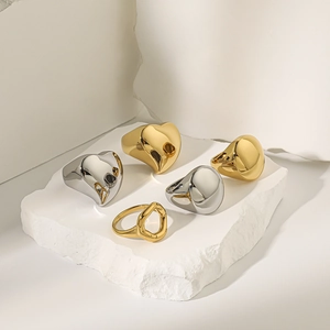 Polished 18K gold and silver rings in heart and pebble shapes on a white stone base