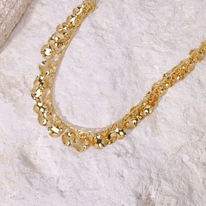Golden stainless steel necklace with curved round disc charms on a stone surface