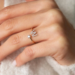 Bague ouverte dorée avec lettre W et zircon sur fond en peluche blanche