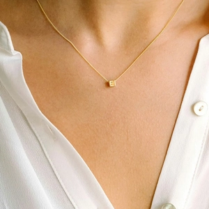 Detail of a gold cube pendant with letter E engraving on a minimalist chain necklace