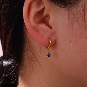 Close-up of 18K gold star earrings with blue glass charms worn by a model