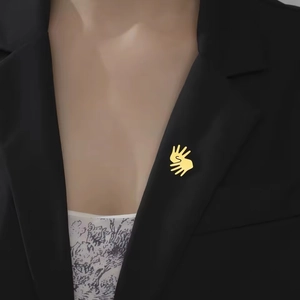 Detail of gold hand-shaped brooch with S letter on black suit lapel for daily wear