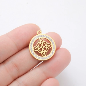 Golden Celtic knot pendant with sparkling crystals held in hand for size reference
