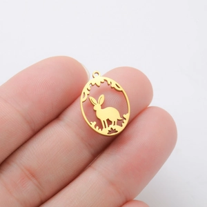 Detailed close-up of a golden hollow bunny oval pendant held between fingers