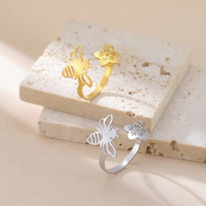 Gold and silver honey bee and flower open rings displayed on travertine stone pedestal