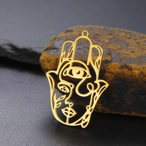 Macro shot of gold Hamsa Hand pendant with Picasso-style abstract face on dark stone