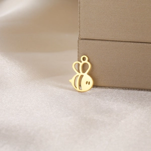 Macro shot of a hollow gold bee charm on silk fabric, showing detailed polished metal finish