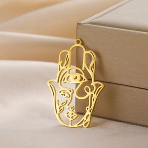 Gold Hamsa hand pendant with artistic cut-out face and eye details on satin fabric