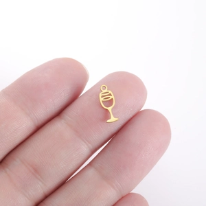 Macro view of a tiny gold-colored wine glass charm on a fingertip for DIY jewelry making