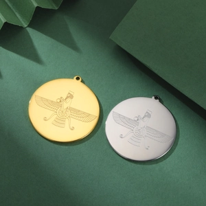Detailed macro view of gold and silver Faravahar pendants on a textured green paper