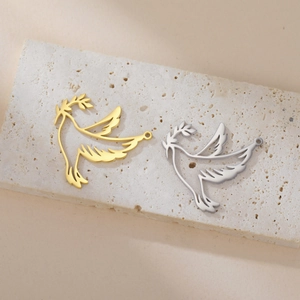 Detail of gold and silver dove of peace charms with olive branch on stone display