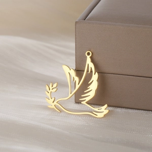 Detailed close-up of golden peace dove pendant with olive branch on silk fabric