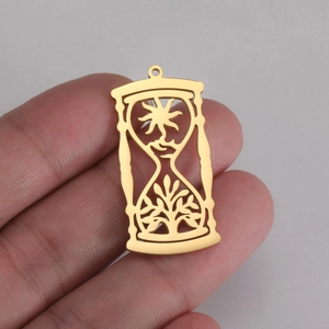 Detailed view of a gold sun and tree hourglass pendant held by hand for scale