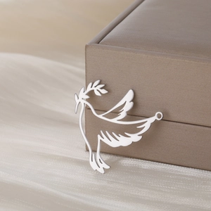 Close-up of polished titanium steel peace dove pendant with olive branch on silk fabric
