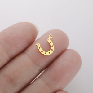 Macro view of gold horseshoe charm with small holes held between fingers for size