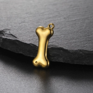 Macro detail of a 3D gold bone-shaped stainless steel pendant on dark stone background