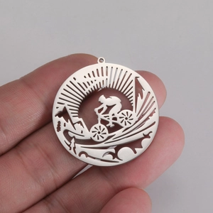 Close-up of a silver hollow metal pendant featuring a cyclist in mountain scenery