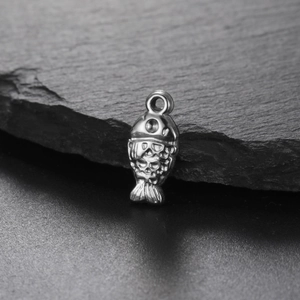 Macro detail of a silver fish pendant with skull patterns on a dark slate background