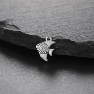 Detailed macro view of silver angel fish charm with wave texture on dark stone