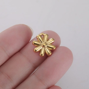 Macro view of a 10mm golden daisy flower pendant charm on a fingertip for DIY jewelry