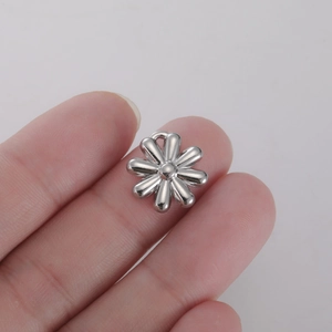 Detailed macro view of a silver daisy flower charm accessory held between fingers for DIY jewelry
