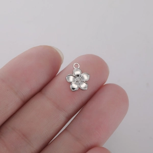Detailed view of a small silver five-petal flower pendant held to show compact size
