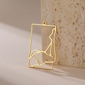 Macro detail of a golden hollow rectangular pendant with minimalist female line art on stone