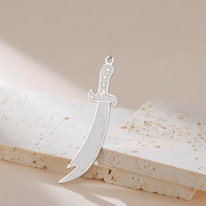 Polished silver stainless steel scimitar sword pendant on beige travertine stone display